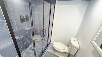 A bathroom with a glass-enclosed shower, a toilet, and a sink.