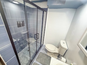 A bathroom with a glass-enclosed shower, a toilet, and a sink.