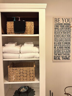 A bathroom with a shelf containing towels and a wall with an inspirational quote. - Daisy Hill Retreat: 4BR/3BA Mins to downtown Asheville and Blue Ridge Parkway! (Swannanoa)
