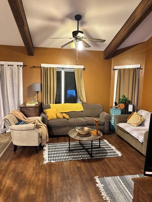 A living room with a ceiling fan, a sofa, a coffee table, and a patterned rug. - Daisy Hill Retreat: 4BR/3BA Mins to downtown Asheville and Blue Ridge Parkway! (Swannanoa)