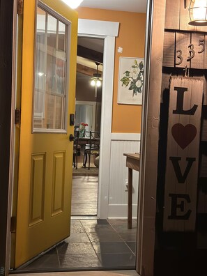 Eine gelbe Tür, die zu einem Raum mit einer weißen Tür, einem gerahmten Bild an der Wand und einem Holzschild mit der Aufschrift 'LOVE' und einem Herz führt.
