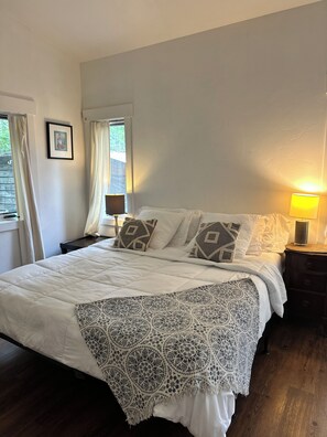 Ein Schlafzimmer mit einem großen Bett, einer Nachttischlampe, einem gerahmten Bild an der Wand und einem Fenster mit Vorhängen.