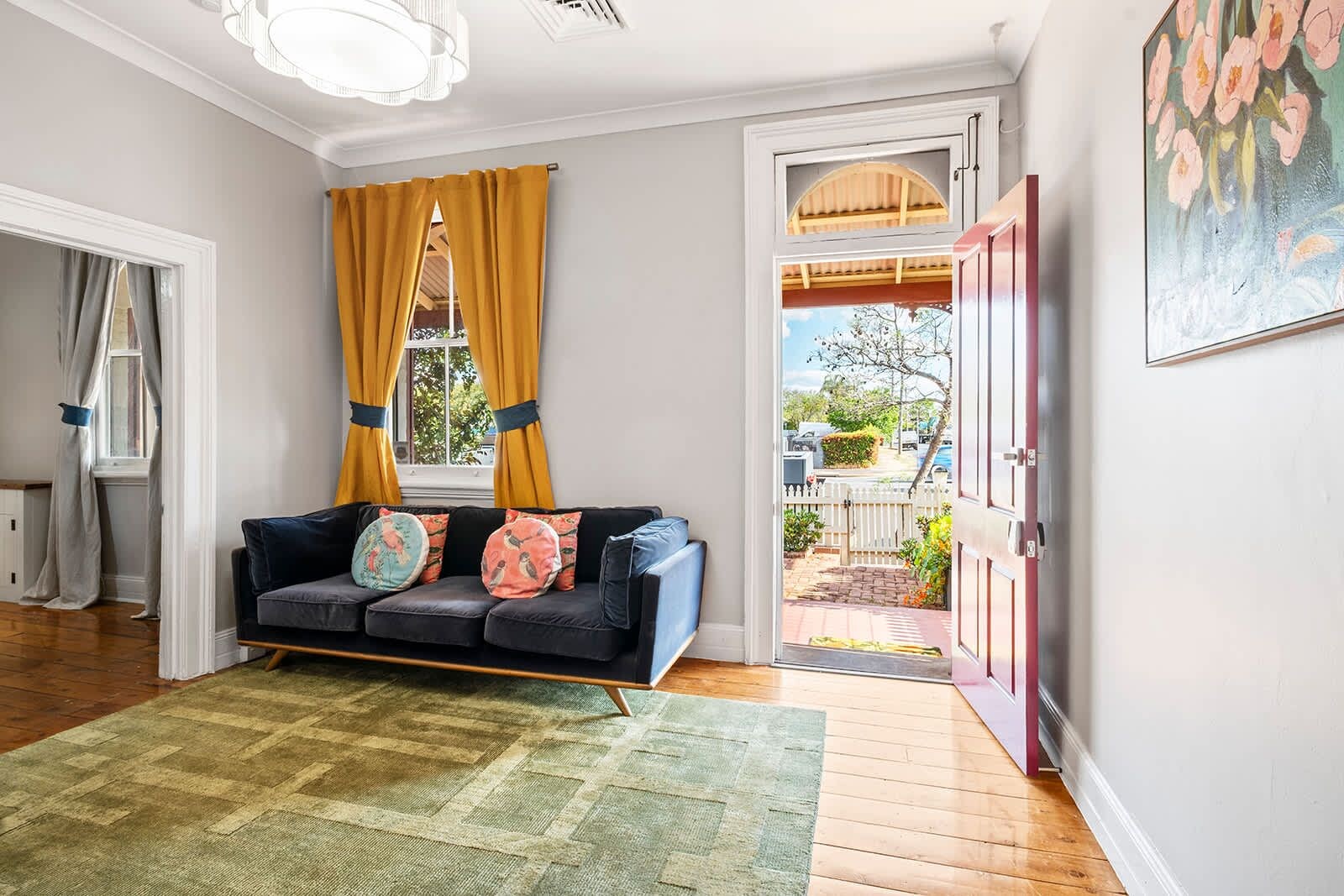 A room with a sofa, a green rug, a window with yellow curtains, and a door leading outside.