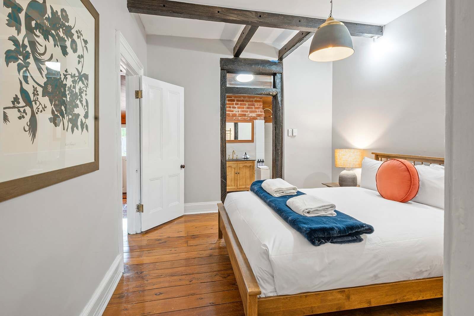 A hotel room with a wooden bed, a nightstand, a lamp, and a bathroom visible through an open door.