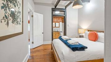 A hotel room with a wooden bed, a nightstand, a lamp, and a bathroom visible through an open door.