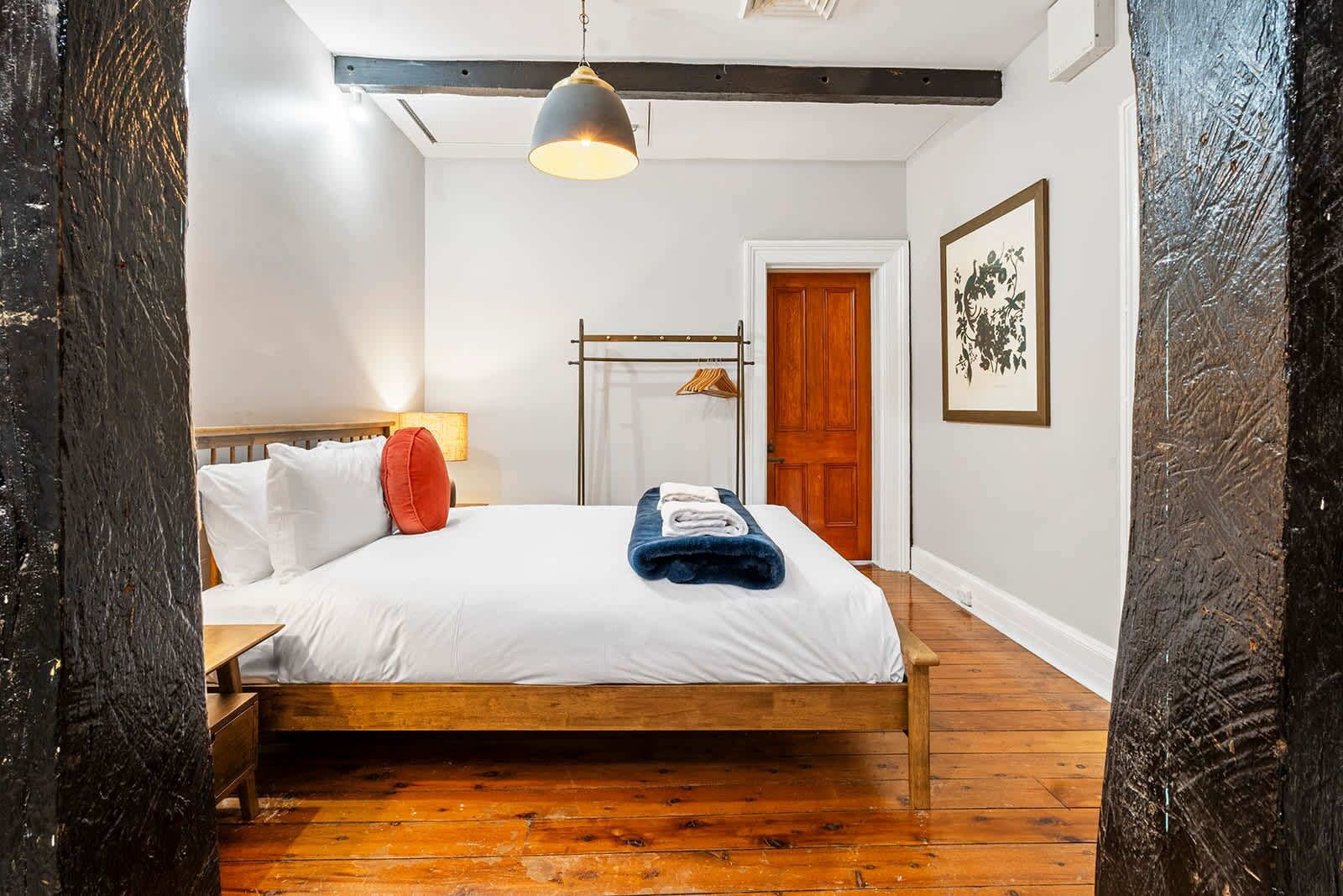 A bedroom with a wooden bed, a hanging light fixture, a wooden door, and a framed artwork on the wall.