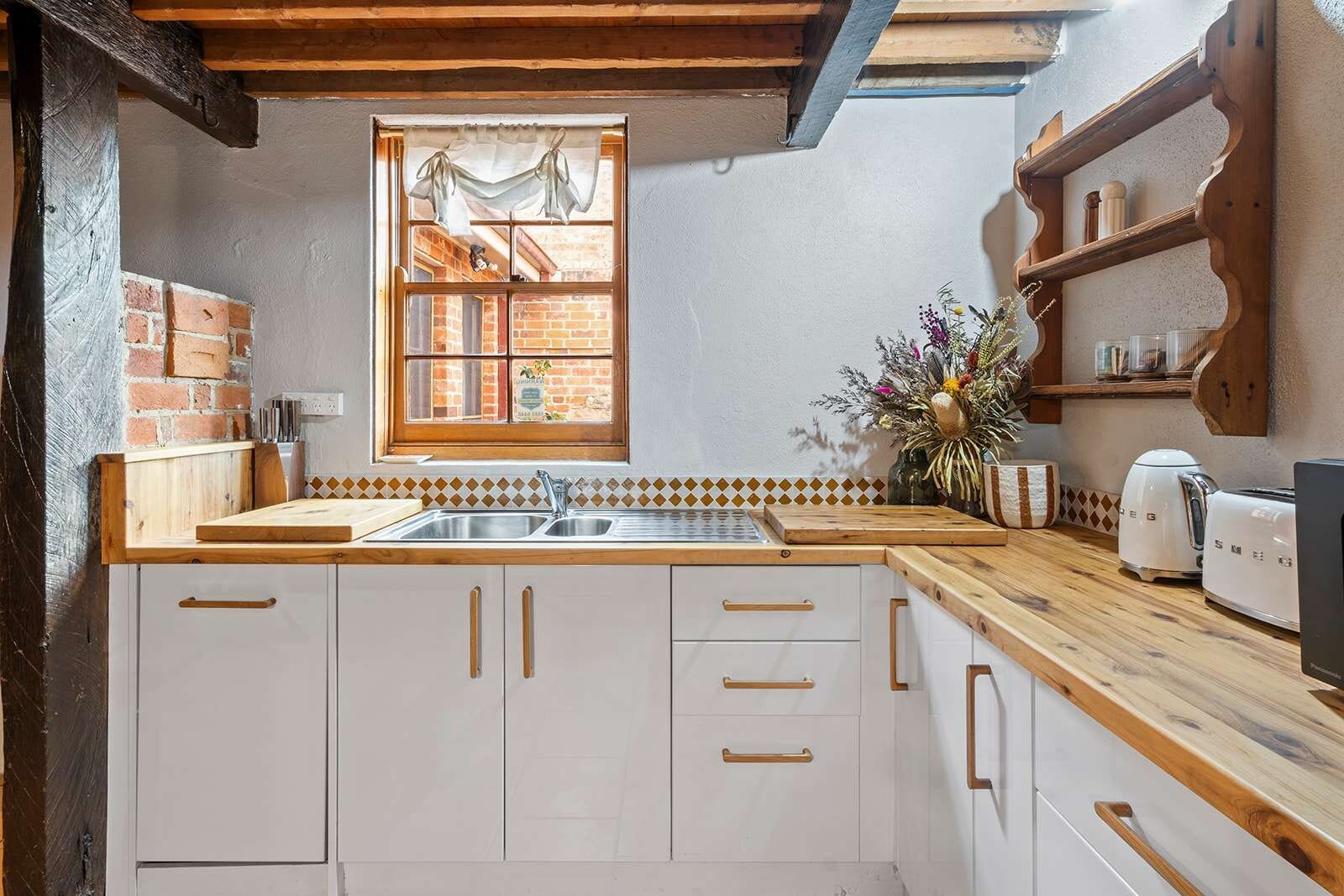 Une cuisine avec un plan de travail en bois, des meubles blancs, un évier et une fenêtre avec des rideaux.