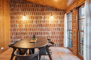 A rustic room with a brick wall, wooden ceiling, and a round table with chairs. - Sheiling 1888  A Honey Home (Dubbo)