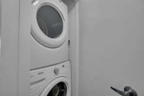 A compact laundry room with a front-loading washing machine and a dryer stacked above it. - The Orient - Spectacular CN Tower Views (Toronto)
