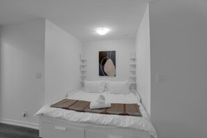 Une chambre à coucher au style minimaliste, avec un lit, des murs blancs et une seule œuvre d’art accrochée au-dessus du lit.