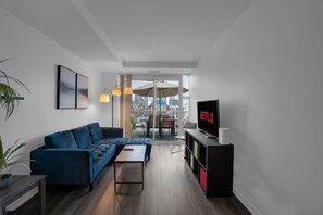 A modern living room with a blue sofa, a coffee table, and a TV on a stand. - The Orient - Spectacular CN Tower Views (Toronto)