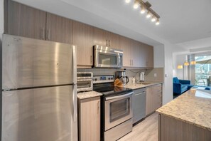 A modern kitchen with stainless steel appliances, wooden cabinets, and a granite countertop. - The Orient - Spectacular CN Tower Views (Toronto)