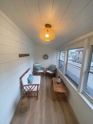 A room with white paneled walls, a wooden floor, a hanging light fixture, a small table with a decorative item, and a view of the street through large windows. - Spacious 6-bedroom, 2 Kitchen, 3 bath house in tranquil Old Orchard Beach (Old Orchard Beach)