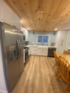 A kitchen with a stainless steel refrigerator, white cabinets, a wooden ceiling, and a dining area with wooden chairs. - Spacious 6-bedroom, 2 Kitchen, 3 bath house in tranquil Old Orchard Beach (Old Orchard Beach)
