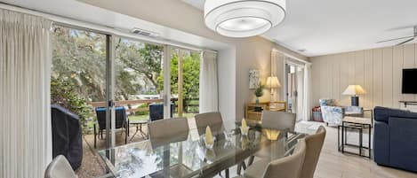 Una sala de estar moderna con una mesa de comedor de vidrio, asientos cómodos, un televisor de pantalla plana y vistas al exterior.