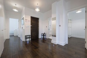 A hallway with wooden flooring, white walls, and a dark wooden door. There are two small tables and a coat rack. - Contemporary 3BR | Near City Centre | FREE Parking (Reading)