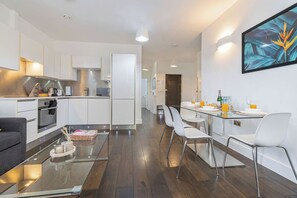 A modern kitchen with white cabinets, stainless steel appliances, and a dining area with a glass table and white chairs. - Contemporary 3BR | Near City Centre | FREE Parking (Reading)