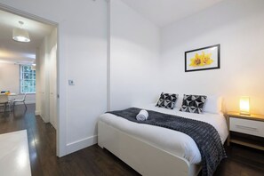 Een slaapkamer met een bed, nachtkastje, lamp en een aan de muur hangend schilderij.