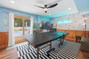 Ein Zimmer mit Tischtennisplatte, Deckenventilator, Neonleuchtreklame und einer Wand mit Sportmotiven.