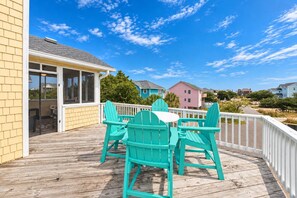 A wooden deck with outdoor seating and a view of colorful houses. - Beach Please OBX | 1,550 ft to the beach | Private Pool, Hot Tub, and Dog Friendly (Corolla)