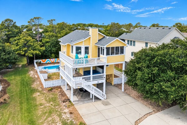 A two-story house with a balcony, a swimming pool, and a well-maintained lawn. - Beach Please OBX | 1,550 ft to the beach | Private Pool, Hot Tub, and Dog Friendly (Corolla)