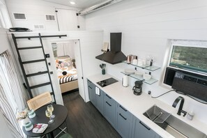 A compact kitchen with a built-in stove, a black range hood, and a window overlooking a natural landscape. - 1BR Fredericksburg retreat with hot tub, fire pit, grill (Fredericksburg)
