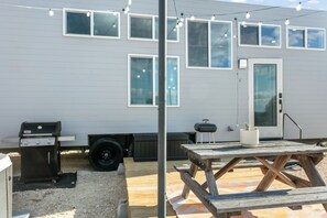 A patio area with a grill, a wooden table, and string lights. - 1BR Fredericksburg retreat with hot tub, fire pit, grill (Fredericksburg)