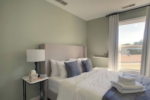 A hotel room with a bed, a bedside table with a lamp, a window with curtains, and a view of the outside. - Indy Gameday House - Downtown - 10 Walk to Lucas Oil Stadium (Indianapolis)