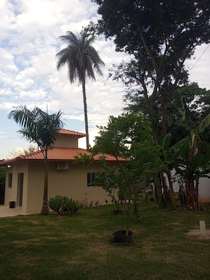 A residential building with a tiled roof, surrounded by a grassy yard and various trees.