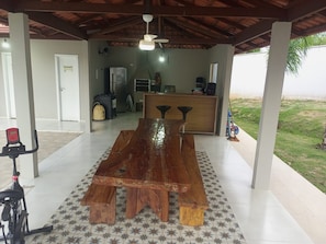 A covered outdoor dining area with a wooden table, a ceiling fan, and a view of a grassy field.