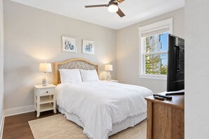 A bedroom with a bed, bedside tables, lamps, a ceiling fan, a TV, and a window. - Selah on 30A | Golf Cart, Pool & Hot Tub, Mins to the Beach (Santa Rosa Beach)