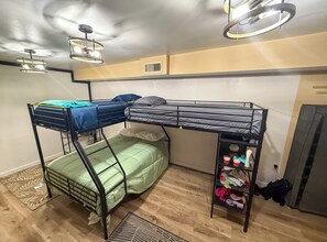 Une chambre avec un lit superposé, un matelas vert, une étagère avec des vêtements et un ventilateur de plafond.