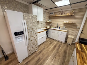 A kitchen with white cabinets, a built-in water dispenser, a wooden countertop, and a backsplash with square tiles. - The Flight Crew Quarters (College Park)