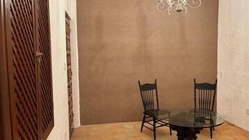 Een eethoek met een glazen tafel, omringd door stoelen, een bruine muur en een gestructureerd plafond.