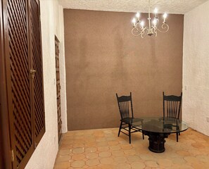 Een eethoek met een glazen tafel, omringd door stoelen, een bruine muur en een gestructureerd plafond.
