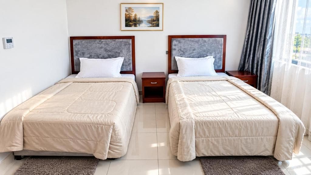 A hotel room with two beds, a nightstand, a painting on the wall, and a window with curtains.