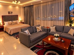 A hotel room with a bed, two sofas, a coffee table, and a TV.