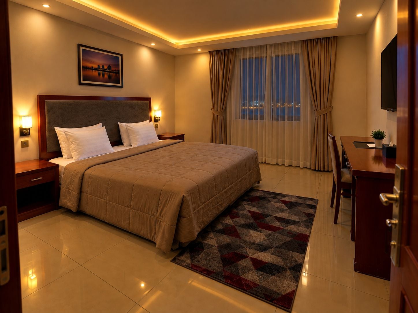 A hotel room with a large bed, a desk with a chair, a nightstand, a lamp, a painting on the wall, and a window with curtains.