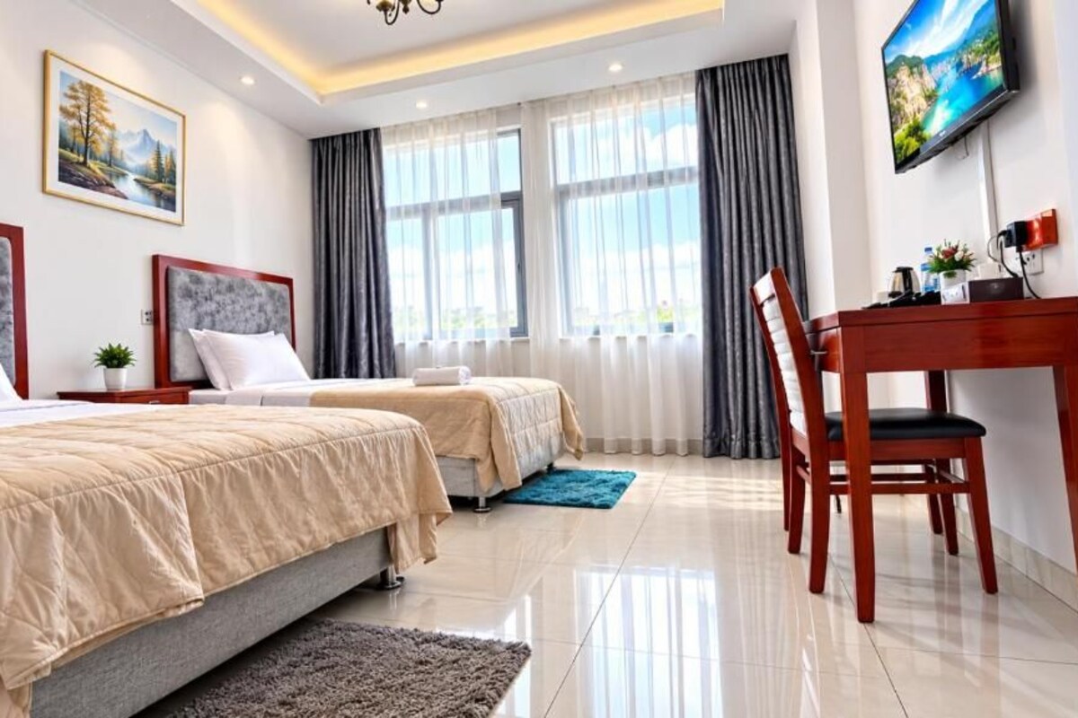 A hotel room with two beds, a desk, a chair, a TV, and a painting on the wall.