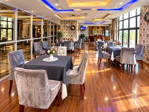 A spacious dining area with multiple tables and chairs, a bar in the background, and large windows allowing natural light. - HOTEL SAINT FRANCOIS DE PAULE  (brazzaville)