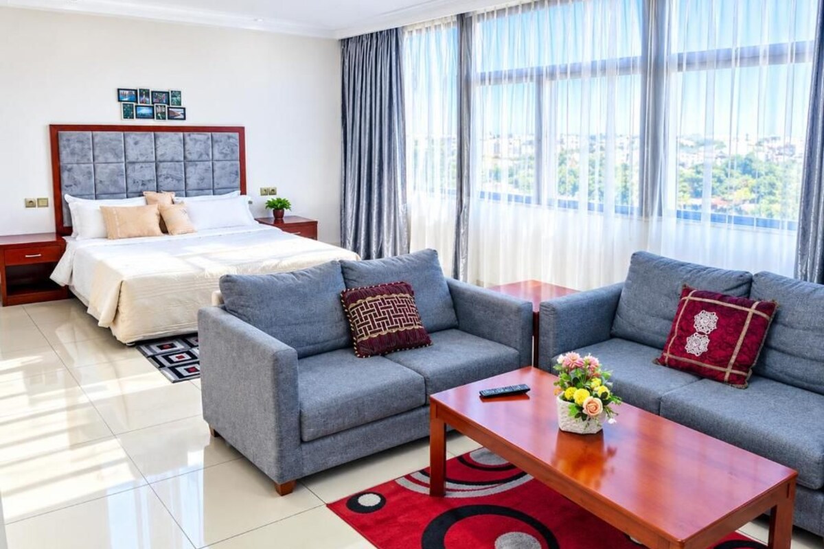 A hotel room with a bed, two sofas, a coffee table, and a view of the city.