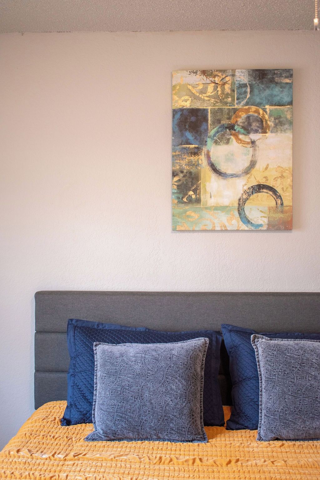 A bed with a grey headboard, a yellow textured bedspread, and three grey pillows.