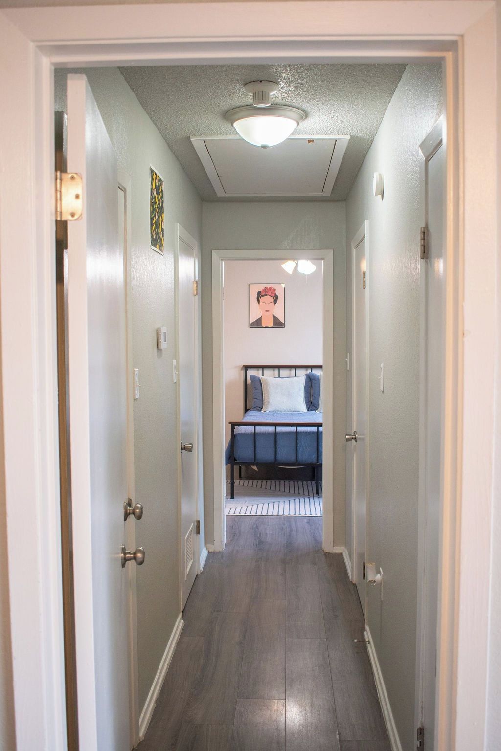 A hallway leading to a bedroom with a bed, a ceiling light, and a wall-mounted picture.