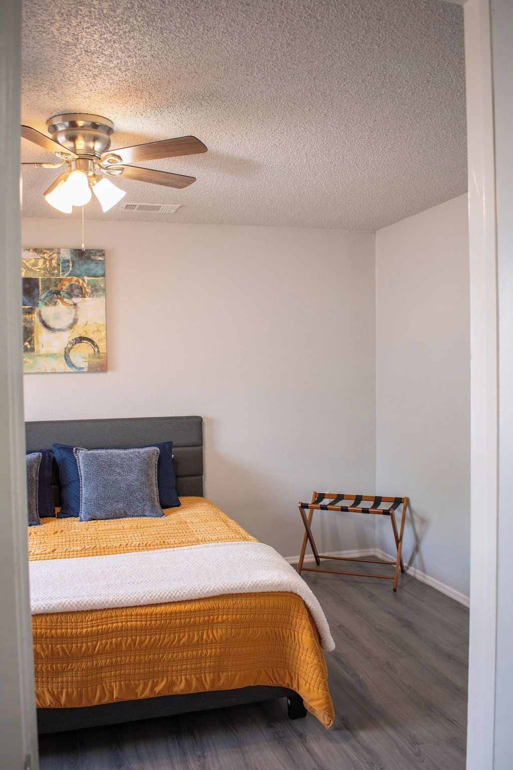 A bedroom with a bed, a ceiling fan, a small table, and a painting on the wall.