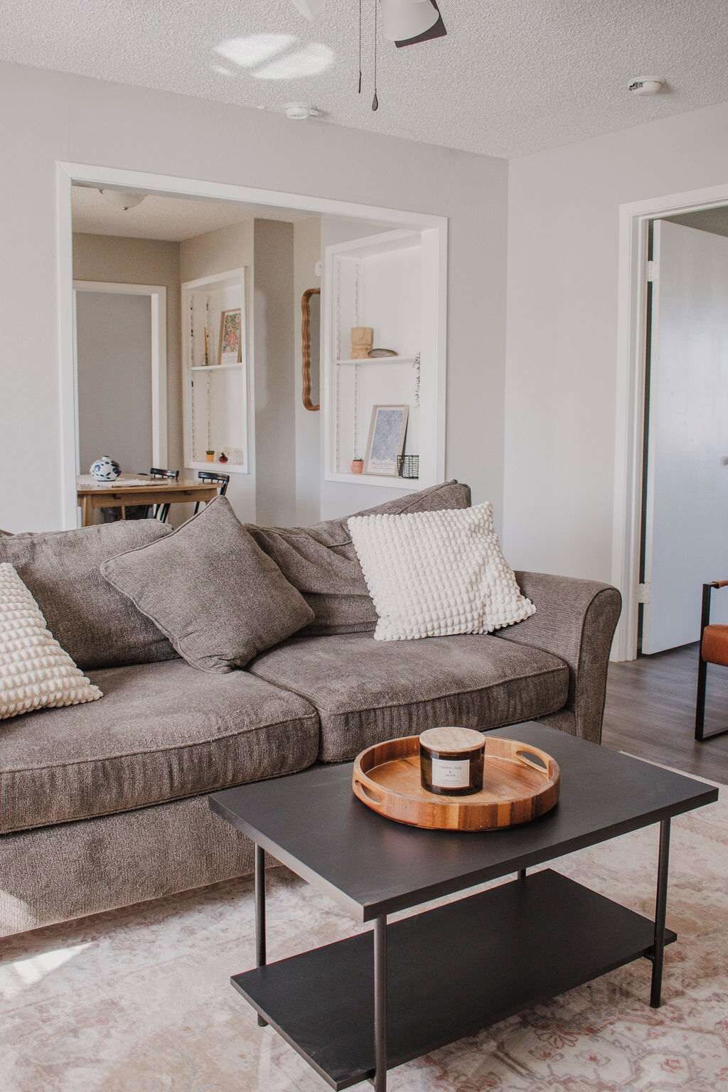 A modern living room with a sectional sofa, a coffee table, and a dining area visible through an open door.