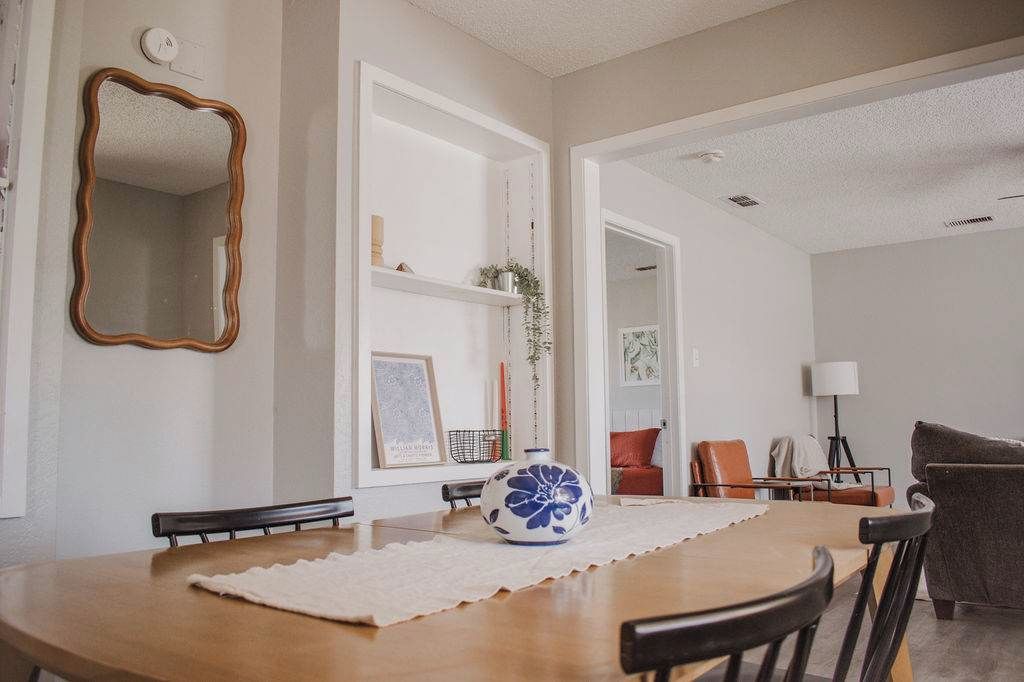 A dining area with a wooden table, chairs, a decorative vase, and a mirror on the wall.