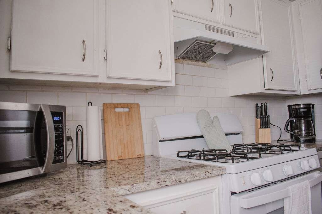 A kitchen with white cabinets, a microwave, a gas stove, and a coffee maker.