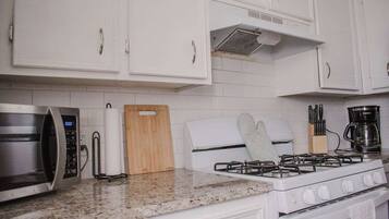 A kitchen with white cabinets, a microwave, a gas stove, and a coffee maker.