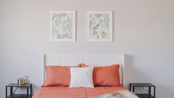 Een slaapkamer met een wit bed, twee kussens, een deken, een plafondventilator en twee ingelijste botanische prints aan de muur.