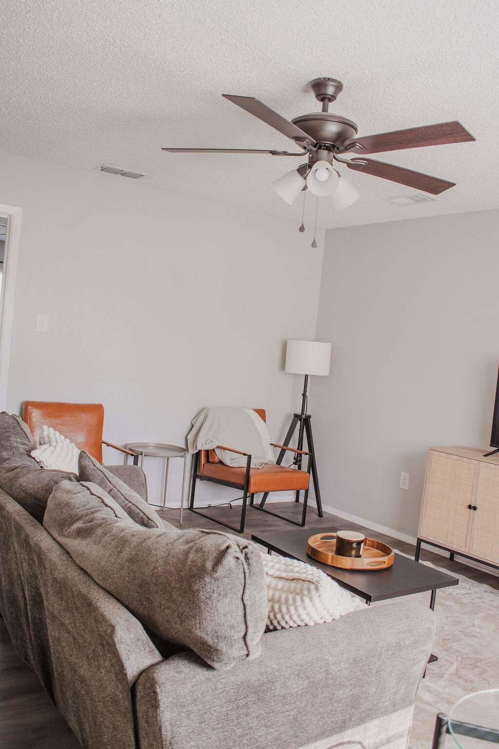 Un salon comprenant un canapé, un fauteuil, une lampe, une table et un ventilateur de plafond.